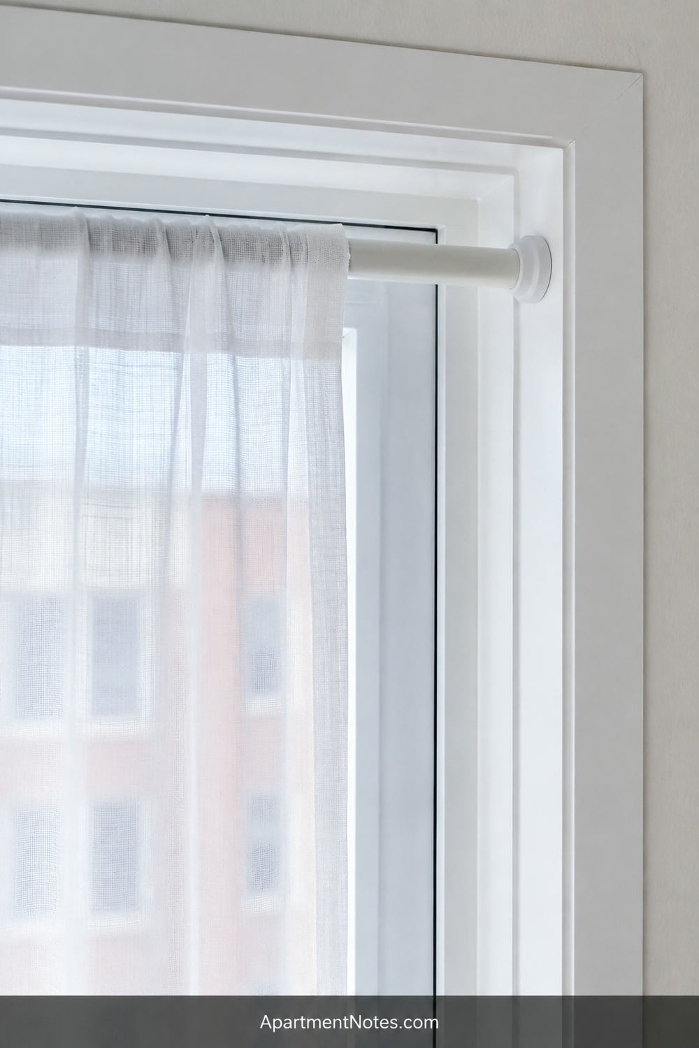 Vertical 2:3 Pinterest editorial photograph close-up of a twist-and-fit tension rod seated inside a white apartment window frame, lightweight sheer curtain hanging straight, daylight and clean trim, no text, no people