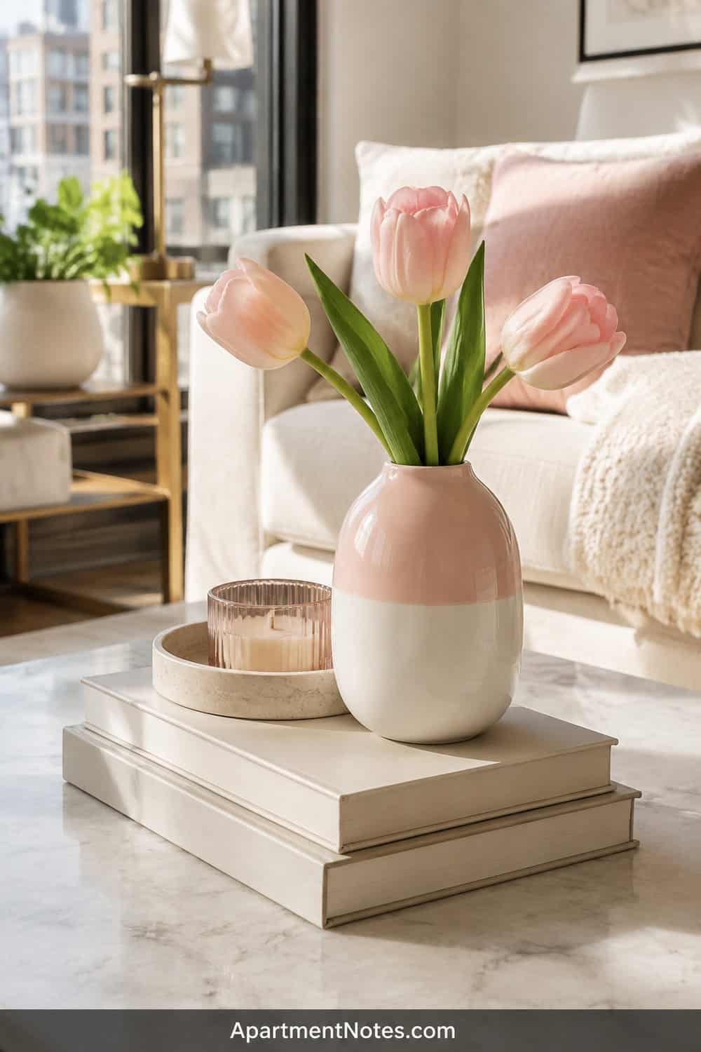 Pinterest editorial coffee table, plain pale-pink and white porcelain bud vase holding three blush tulips, stacked neutral books and a small candle tray, sunlit apartment living room, vertical 2:3, no chinoiserie patt...